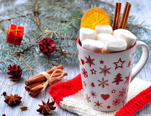 chocolate or cocoa drink with marshmallows and cinnamon in a Christmas cup on the background of blue spruce