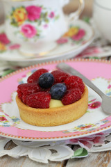 Delicious crunchy tartelette with custard, fresh raspberries and blueberries with cup of tea
