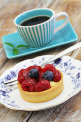 Crunchy tartelette with fresh fruit and cup of coffee on rustic wooden surface

