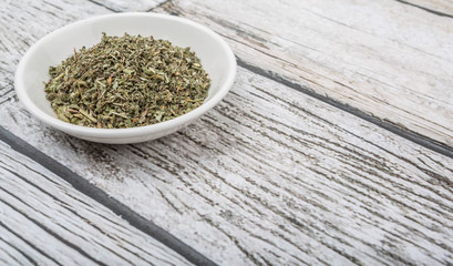 Dried lemon balm leaves in white bowl over wooden background