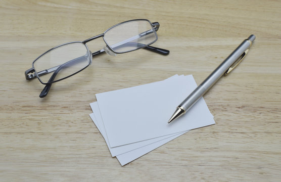 Blank business card with pencil and glasses on wooden table