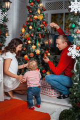 Young family with baby girl decorates the Christmas tree toys