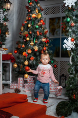 Baby girl standing near the Christmas tree and holding a toy