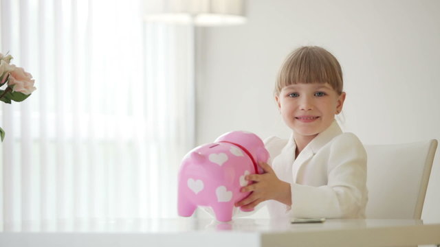 Girl sitting at table and holding piggy bank