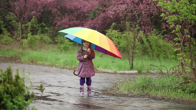 Little girl with an umbrella in the rain in the park. Child spinning with an umbrella in his hand