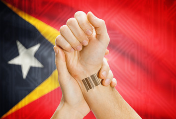 Barcode ID number on wrist and national flag on background - East Timor