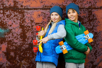 Smiling boy and girl holding color plastic penny boards or skateboards outdoor