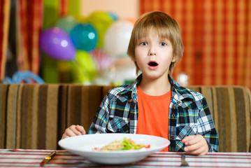 confused boy with knife and fork in front of salad. Teenager eating at cafe - 95411952