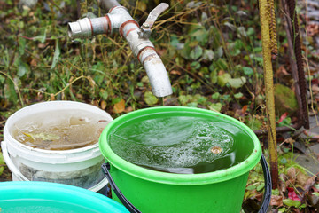 Water dripping from a faucet in a bucket in the garden.