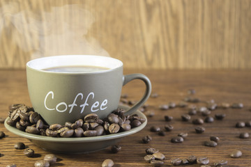 Cup of coffee with beans standing on a wooden table. Blurred, focus on mug