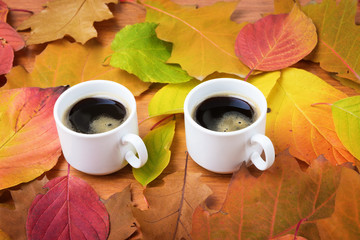 Coffee cups with autumn leaves on wooden background