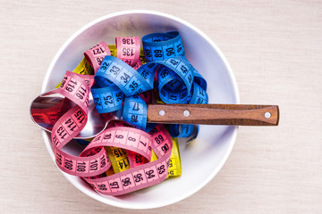 Many colorful measuring tapes in bowl on table