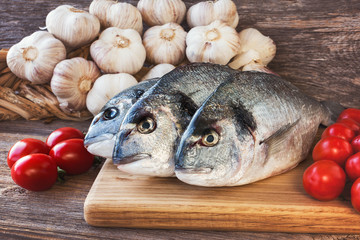 Fresh dorada fish on wooden cutting board with vegetables. Toned