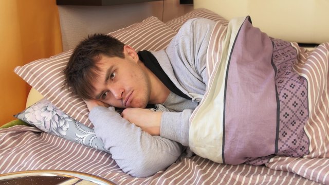 Young man lying, looking and thinking in bed