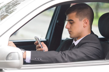 Portrait of a young businessman using phone while driving a car