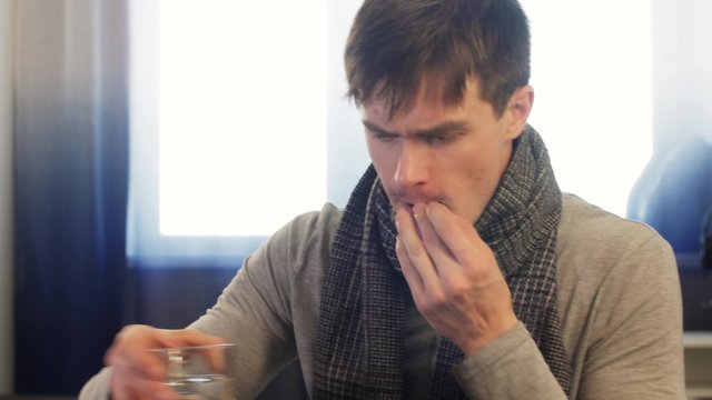 Sick man taking pill while sitting. Static shot