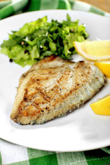 Dish of fish fillet with greens and lemon on plate close up