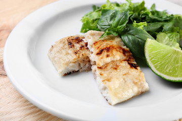 Dish of fish fillet with greens and lime on table close up