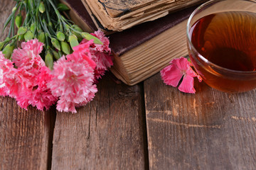 Old books with beautiful flowers and cup of tea on wooden table close up