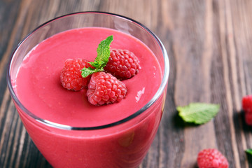 Glass of raspberry milk shake with berries on wooden table close up