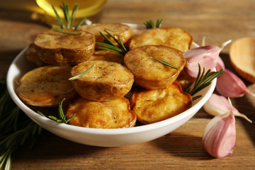 Delicious baked potato with rosemary in bowl on table close up