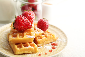 Sweet homemade waffles with fresh strawberries on plate, on light background