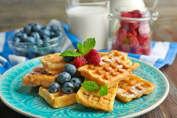 Sweet homemade waffles with forest berries and sauce on table background