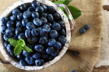 Tasty ripe blueberries with green leaves in bucket on table close up