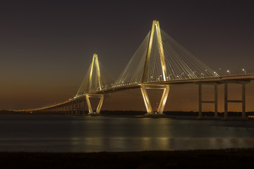 Arthur Ravenel Jr. Bridge illuminated aginst a darkening dusk sky.  The bridge carries eight lanes of traffic over the Cooper River between Charleston and Mount Pleasant, SC.
