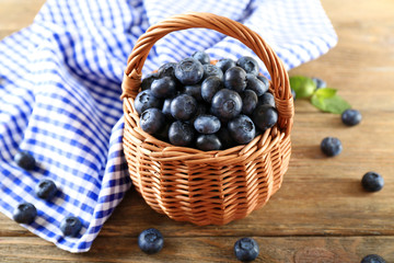 Tasty ripe blueberries with green leaves in basket on wooden table close up