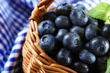 Tasty ripe blueberries with green leaves in basket close up