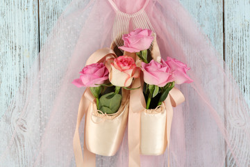 Decorated ballet shoes with roses in it hanging on blue wooden background