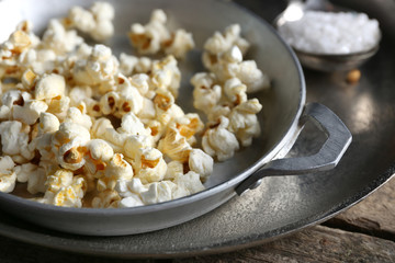 Salted popcorn in a metal bowl with cup of corns on wooden table, close up