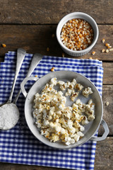 Salted popcorn in a metal bowl with cup of corns on checked cotton napkin on wooden table