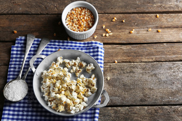 Salted popcorn in a metal bowl with cup of corns on checked cotton napkin on wooden table