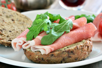 Gesundes Frühstück - Rohschinken mit Rucola und Brötchen auf Teller / Nahaufnahme - Makro