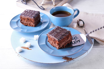 Served table with a cup of tea and chocolate cakes on blue plates close-up