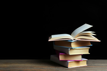 Pile of different books on wooden table against black background