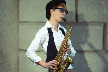 Girl with saxophone outside near the brick wall