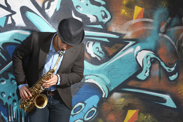 Fototapeta na wymiar Saxophone player on graffiti wall background