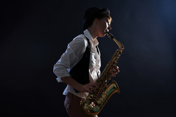 Plakat Attractive woman plays saxophone on dark background