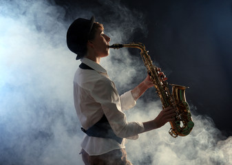 Obraz na płótnie Canvas Attractive woman plays saxophone on dark background in the smoke