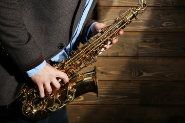 The musician with sax on wooden background, close up