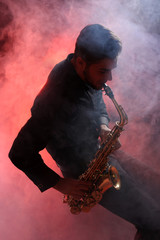 Fototapeta na wymiar Young man professionally plays sax in red smoke