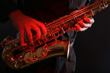 Musician in black shirt with sax on dark background, close up