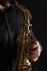 Obraz premium Musician in black shirt with sax on dark background, close up