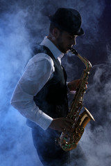 Naklejka na ściany i meble Elegant saxophonist plays jazz on dark background in blue smoke