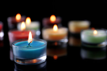 Obraz na płótnie Canvas Colourful alight candles in a row on black background, blurred
