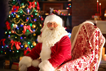 Fototapeta na wymiar Santa Claus sitting in comfortable chair near fireplace at home