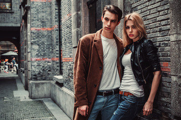 Young trendy man and woman posing in brick walls street  